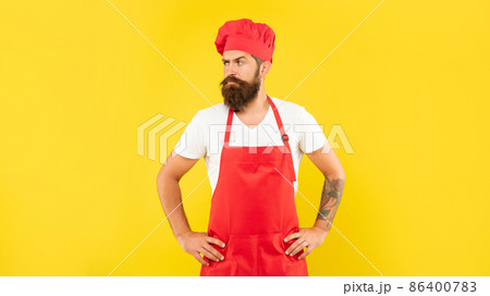 Confident man in red toque and apron looking aside with arms akimbo yellow background, chef 86400783
