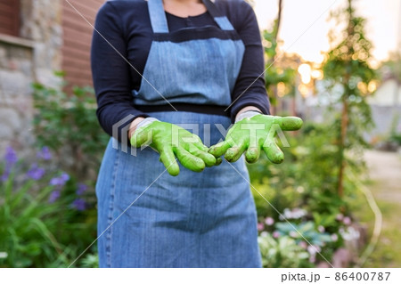 Closeup of gardener woman's hands in gardening gloves, spring garden background. Closeup of gardener woman's hands in gardening gloves, spring garden background. 86400787