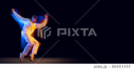 Dynamic portrait of male hip-hop dancer dancing isolated on dark background in mixed neon light. Youth culture, hip-hop, movement, style and fashion, action. Dynamic portrait of male hip-hop dancer dancing isolated on dark background in mixed neon light. Youth culture, hip-hop, movement, style and fashion, action. 86401435
