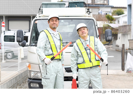 誘導棒を持つ交通誘導をする作業服姿の男性達 86403260