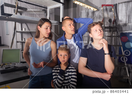 Close-knit family with children thinks, trying to find a solution to the puzzle in the quest room, to get out of there 86403441