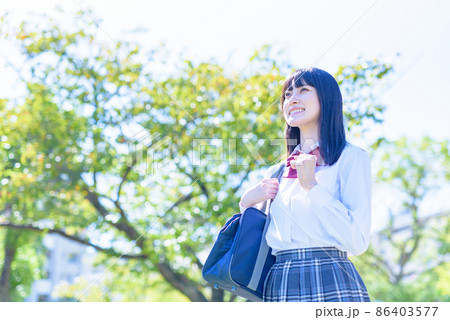 綺麗な新緑の公園で空を見上げてガッツポーズする女子高校生　通学　登校　　将来進路　　昼イメージカラー 86403577