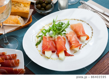 Spanish dish - rolls of iberian jamon stuffed with melon served with arugula Spanish dish - rolls of iberian jamon stuffed with melon served with arugula 86403595