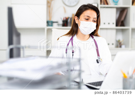 Woman doctor in protective mask sitting at workplace with computer in office 86403739