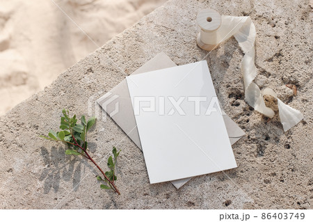 Summer wedding stationery mock-up. Blank greeting card, invitation. Envelope and silk ribbon in sunlight. Green lentisk branch. Beige concrete background in sunlight. Blurred sandy beach. Top view. Summer wedding stationery mock-up. Blank greeting card, invitation. Envelope and silk ribbon in sunlight. Green lentisk branch. Beige concrete background in sunlight. Blurred sandy beach. Top view. 86403749