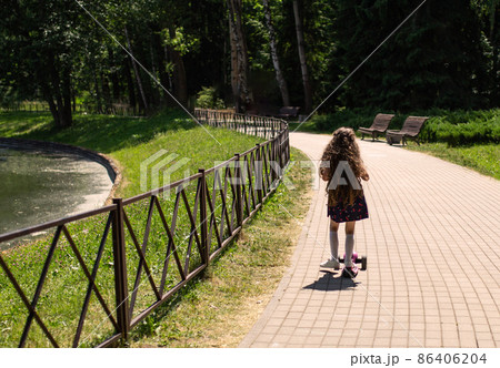Little girl is riding a scooter in the park 86406204