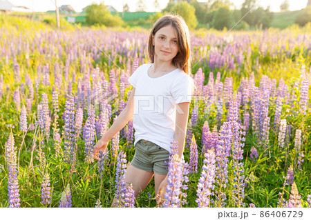 Happy teenage girl smiling outdoor. Beautiful young teen woman resting on summer field with blooming wild flowers green background. Free happy kid teenager girl, childhood concept 86406729
