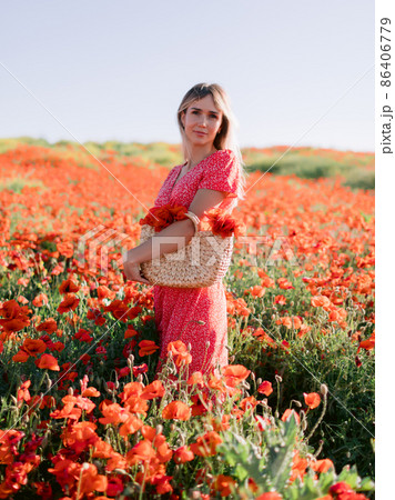 Caucasian blonde woman in a poppy field. Woman in red dress and handbag with wild flowers Caucasian blonde woman in a poppy field. Woman in red dress and handbag with wild flowers 86406779