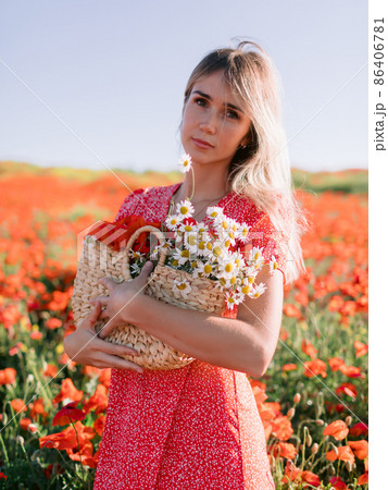 Caucasian blonde woman in a poppy field. Woman in red dress and handbag with wild flowers 86406781