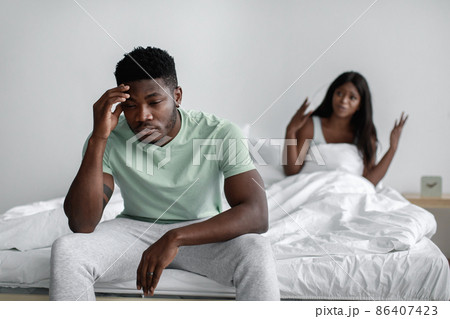 Sad millennial african american woman sits on bed swear her offended husband in bedroom interior Sad millennial african american woman sits on bed swear her offended husband in bedroom interior 86407423