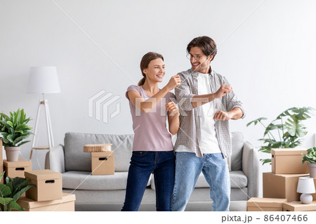 Satisfied caucasian young male and female have fun, dancing in living room interior with cardboard boxes 86407466