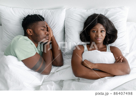 Displeased angry funny young african american lady suffering from snoring, sleeping man Displeased angry funny young african american lady suffering from snoring, sleeping man 86407498