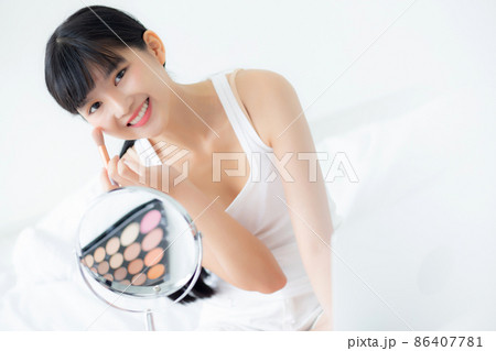 Beautiful young asian woman applying brush on cheek makeup of cosmetic looking mirror on bed. Beautiful young asian woman applying brush on cheek makeup of cosmetic looking mirror on bed. 86407781