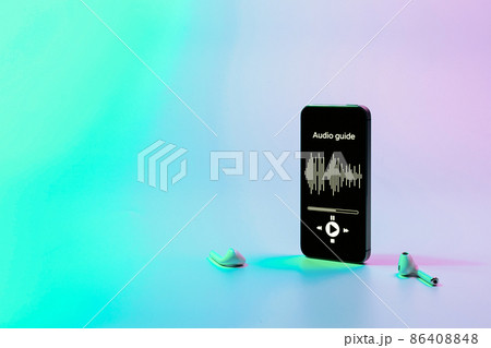 Audio guide online app on digital mobile smartphone screen with music headphones on neon background. Devices for listening audioguide to excursions. 86408848
