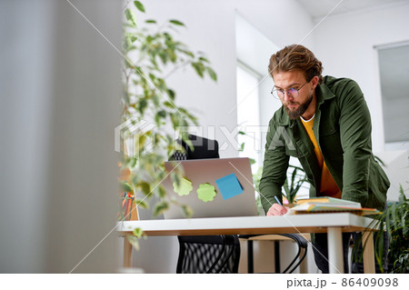 Bearded confident male stand behind office desk with laptop thinking working alone 86409098