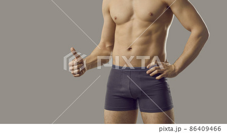 Attractive masculine young macho man in boxer underwear shows OK thumb up standing isolated on grey background. Shirtless handsome male with fit muscular body advertising viagra or impotence treatment 86409466
