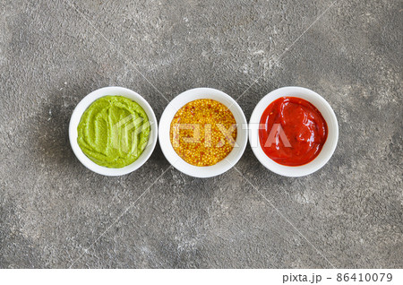 Three types of sauces, french mustard, ketchup and guacamole on a grey background. Three types of sauces, french mustard, ketchup and guacamole on a grey background. 86410079