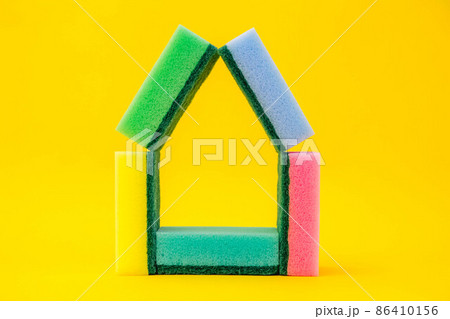 Multicolored sponges for cleaning folded in the shape of a house on a yellow background. Space for text Multicolored sponges for cleaning folded in the shape of a house on a yellow background. Space for text 86410156