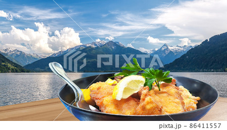Traditional austrian food (Wiener schnitzel) against Zell am see village with lake in Austria 86411557