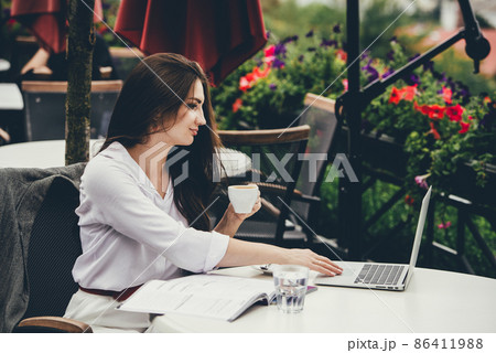 Young freelancer woman using laptop computer sitting at cafe table. Smiling woman working online or studying and learning while using notebook. 86411988