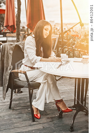 Smiling young dark-haired businesswoman makes notes in a notebook in a cafe on a summer day. Business, e-learning, freelance concept. laptop on a table 86412001