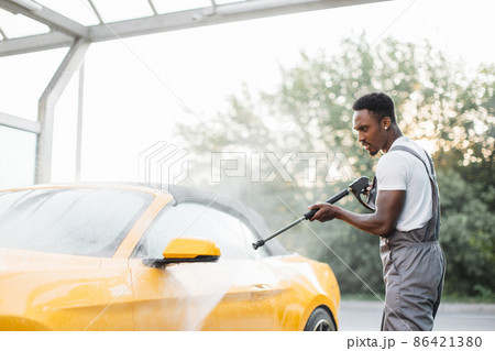 Washing outside rearview car mirror with high pressure water at self car wash service outdoors. Washing outside rearview car mirror with high pressure water at self car wash service outdoors. 86421380