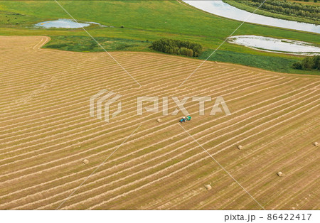 4K Aerial View Tractor Collects Dry Grass In Straw Bales In Wheat Field. Special Agricultural Equipment. Hay Bales, Hay Making. 86422417