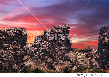 Surrealistic composition of the Devil's Wall near Thale in Saxony-Anhalt, Germany in front of a red and purple evening sky, rib of limestone on the edge of the Harz Mountains Surrealistic composition of the Devil's Wall near Thale in Saxony-Anhalt, Germany in front of a red and purple evening sky, rib of limestone on the edge of the Harz Mountains 86423450