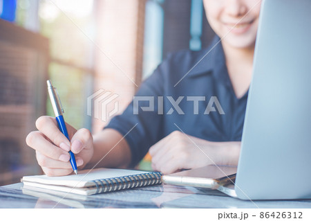 Woman hand writing on a notepad with a pen and use a laptop computer in the office. 86426312