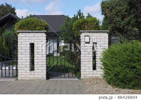 Close-up of a metal gate and a brick fence. Entrance to the property, house. Close-up of a metal gate and a brick fence. Entrance to the property, house. 86426604