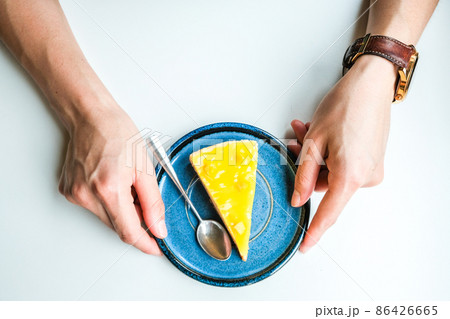 Top view of woman hands touching a plate with sliced piece of homemade Pineapple cheesecake on isolated white table. 86426665