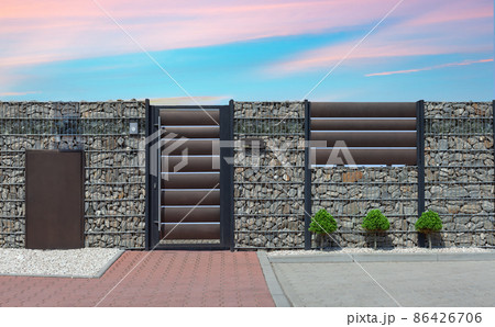 Closed metal gate to property, part of modern stone wall fence with mailbox at street 86426706