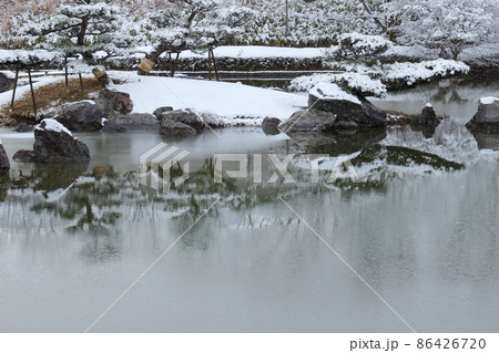 雪の降る日に薄氷の張った公園の池 86426720