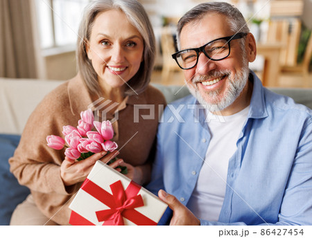Loving man husband giving flowers and present gift box for Valentine's day to happy wife Loving man husband giving flowers and present gift box for Valentine's day to happy wife 86427454