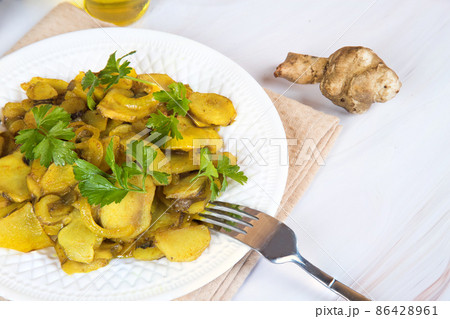 Close - up of a plate with roasted jerusalem artichoke and parsley leaves on the table . Close - up of a plate with roasted jerusalem artichoke and parsley leaves on the table . 86428961
