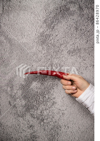 Pointing gesture of a woman's hand with hot pepper.Vertical arrangement Pointing gesture of a woman's hand with hot pepper.Vertical arrangement 86428970