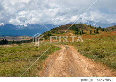 Summer path through mountains. Trekking mountain trail. Atmospheric rural minimalist alpine landscape with stony footpath among grasses in highlands. Pathway uphill. Rainy season. 86429051