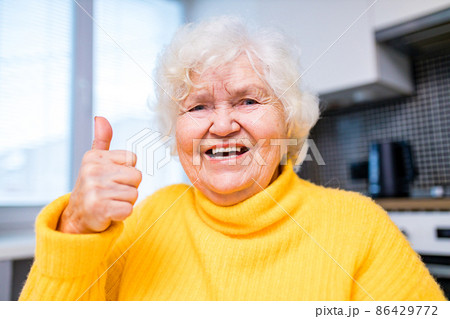 Senior woman showing thumbs up in in living room Senior woman showing thumbs up in in living room 86429772