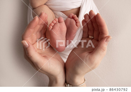The palms of the mother are holding the foot of the newborn baby in a white blanket. Feet of the newborn on the palms of the parents. Studio macro photo of a child's toes, heels and feet. The palms of the mother are holding the foot of the newborn baby in a white blanket. Feet of the newborn on the palms of the parents. Studio macro photo of a child's toes, heels and feet. 86430792
