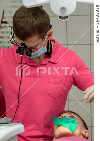 The dentist installs a rubber dam and a clamp for the treatment of a diseased tooth. 86432339