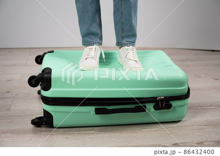 Woman standing with her feet on a suitcase. 86432400