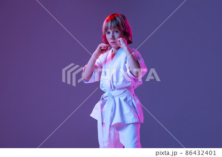 Studio shot of sportive kid, male taekwondo, karate athletes in doboks posing isolated on purple background in neon. Concept of sport, martial arts 86432401