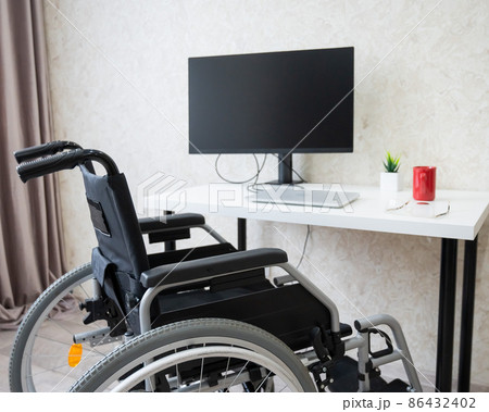 Workplace for a disabled person. Wheelchair at the table with a computer.  86432402