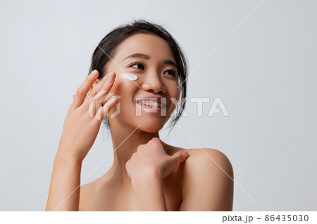 Cropped portrait of young smiling woman doing skincare routine, moisturizing face with special cream 86435030