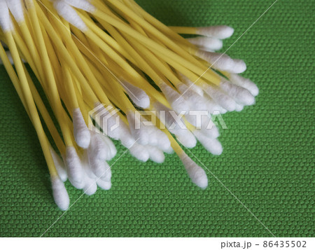 A large number of cotton swabs on a green background, a close-up shot. Cotton swabs or cotton buds. They are most commonly used for ear cleaning. A large number of cotton swabs on a green background, a close-up shot. Cotton swabs or cotton buds. They are most commonly used for ear cleaning. 86435502