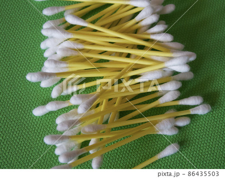 A large number of cotton swabs on a green background, a close-up shot. Cotton swabs or cotton buds. They are most commonly used for ear cleaning. A large number of cotton swabs on a green background, a close-up shot. Cotton swabs or cotton buds. They are most commonly used for ear cleaning. 86435503