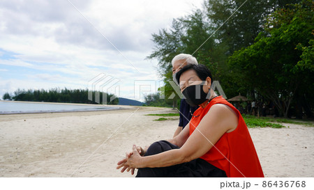 Asian senior couple with mask relax sitting on beach log white sand landscape and beautiful sea Asian senior couple with mask relax sitting on beach log white sand landscape and beautiful sea 86436768