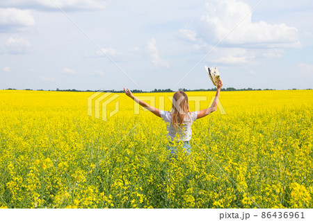 A girl stands in a yellow field with her back and holds a hat A girl stands in a yellow field with her back and holds a hat 86436961