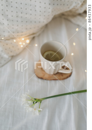 Cup of lemon tea, daffodil flower and accessorries on bed. Breakfast in bed. Morning. Spring.  86437933