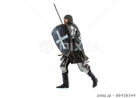Portrait of concentrated man, medieval warrior in chain armor with sword and shield attacking enemy isolated over white studio background 86438344